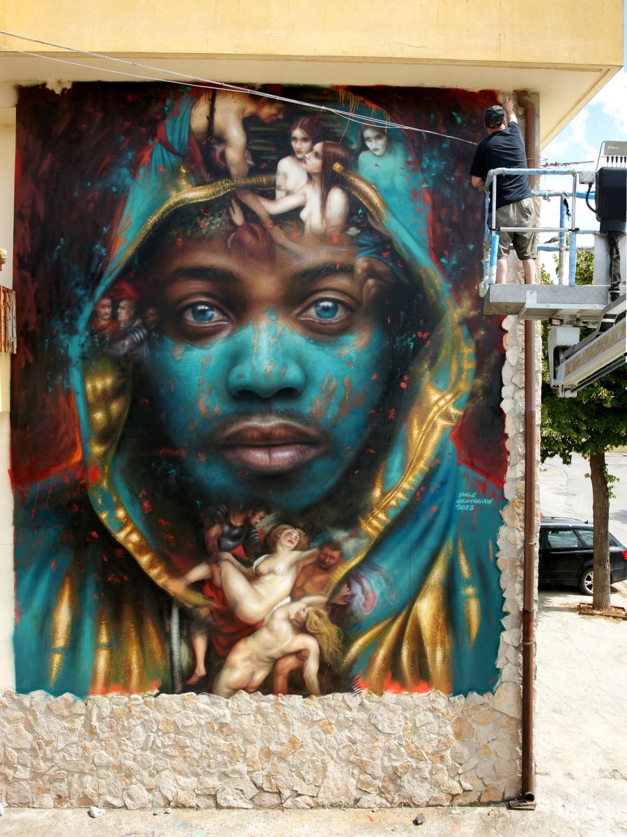 Street artist Dale Grimshaw working on top of a cherry picker is dwarfed by the giant street art mural of a face he is creating
